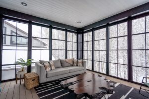 Enclosed sunroom with sofa, large windows, and modern decor.