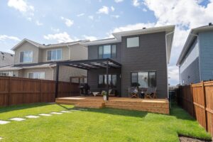 Modern backyard patio cover with wooden deck and green lawn.